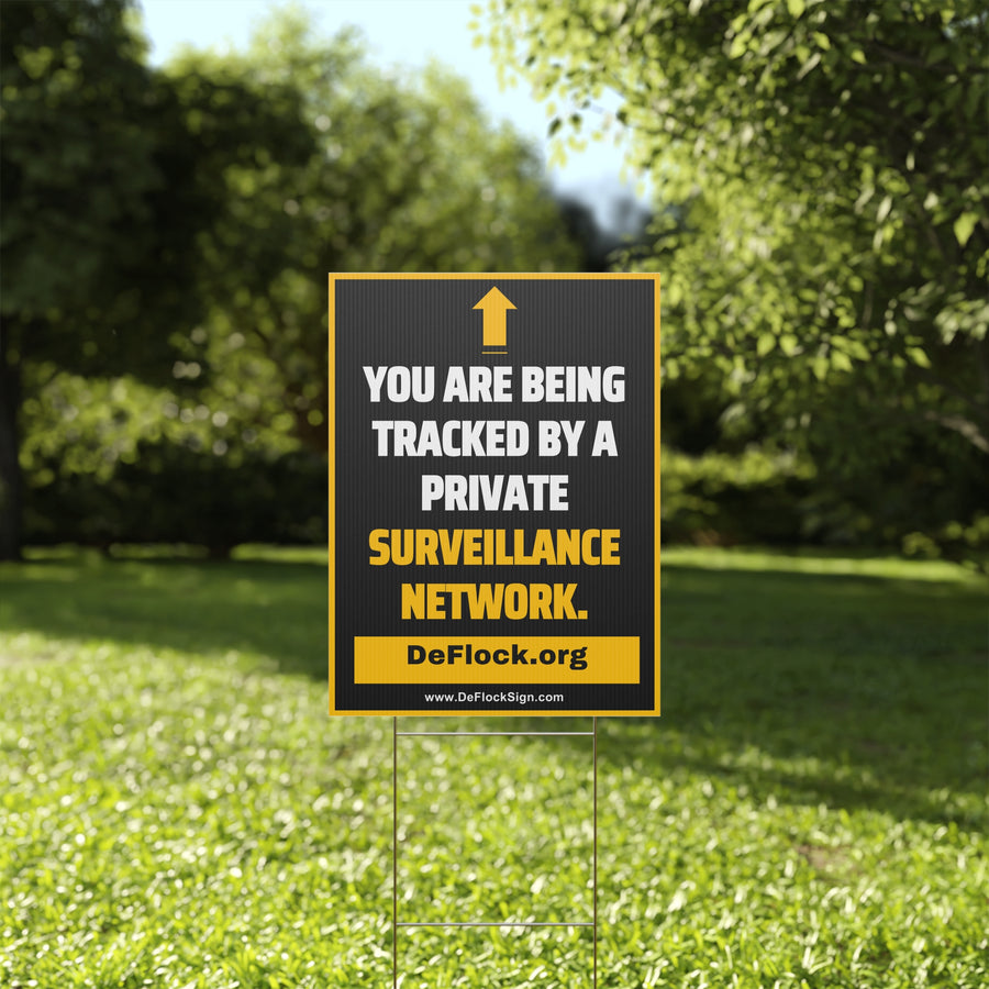 Yard sign with an arrow pointing upwards, and a message that says "You are being tracked by a private surveillance network" to indicate that above the sign is a surveillance camera.